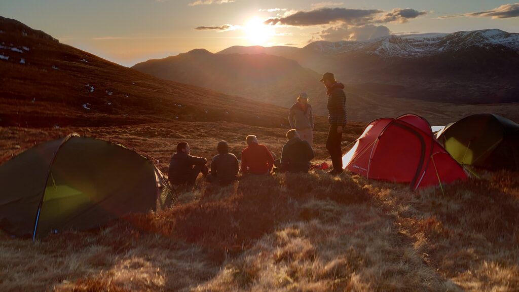 An image of people camping in the mountains as the sun sets on a DofE expedition