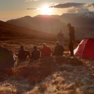 An image of people camping in the mountains as the sun sets on a DofE expedition