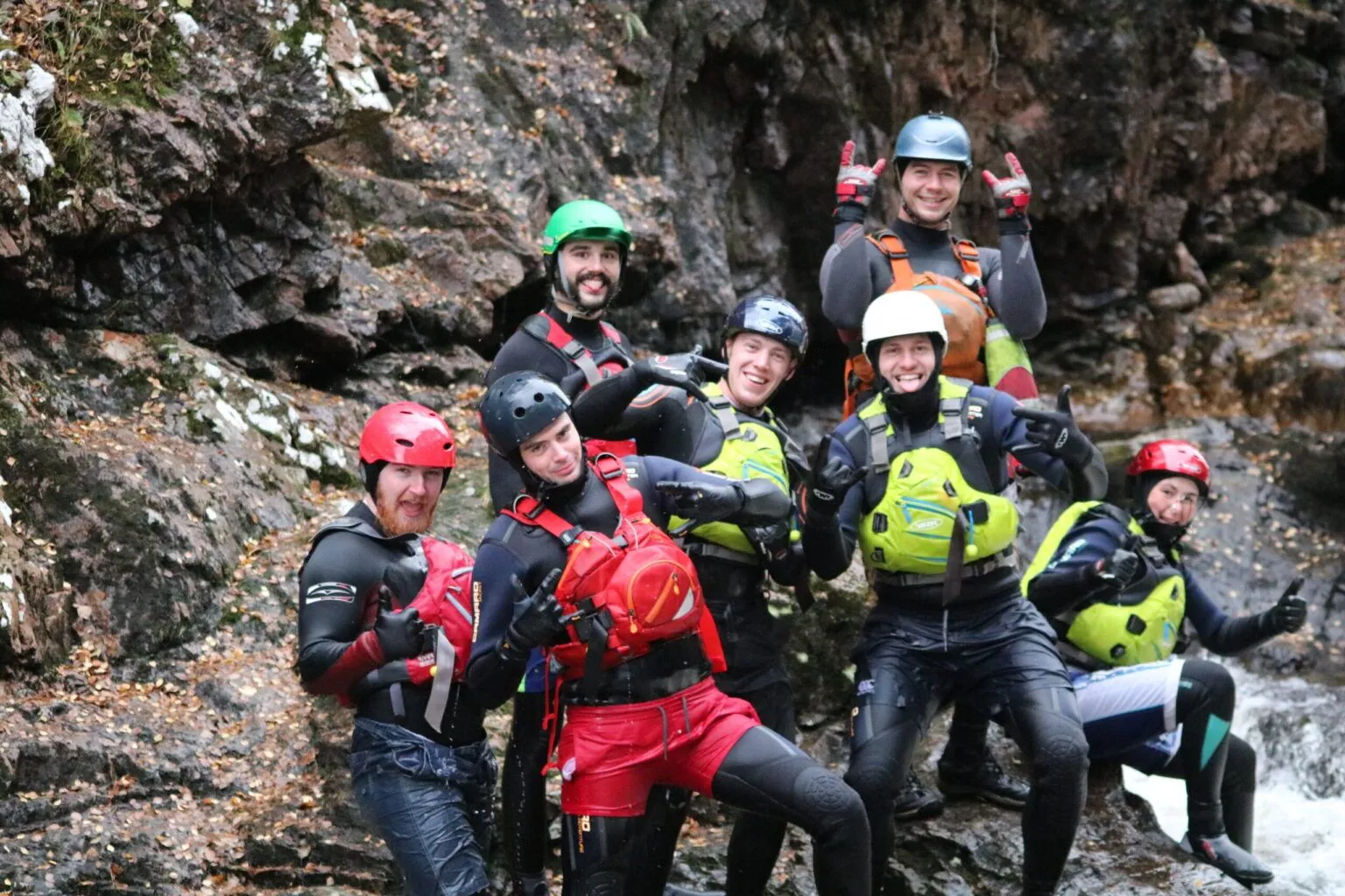 A group of people taking part in an outdoor instructor training course, wearing safety gear, standing on rocks by a river,