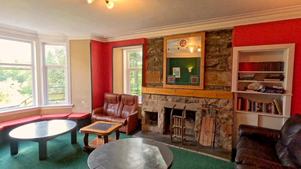 Image of a living/social area within the Craigower Lodge Outdoor Centre with sofas, tables, bookcases, and fireplace.